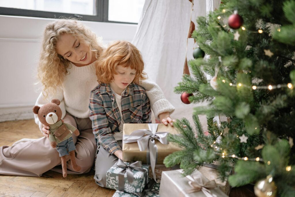 A joyful mother and child unwrapping gifts by the Christmas tree, creating warm family memories.