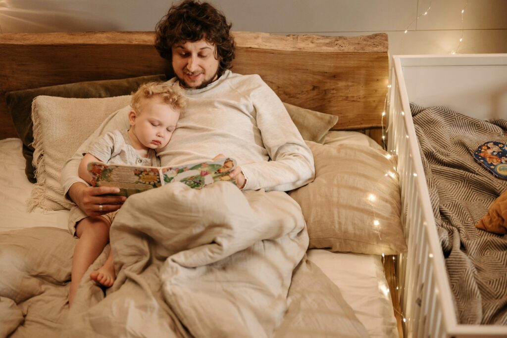 A father and child share a cozy bedtime story in bed, surrounded by warm lighting.
