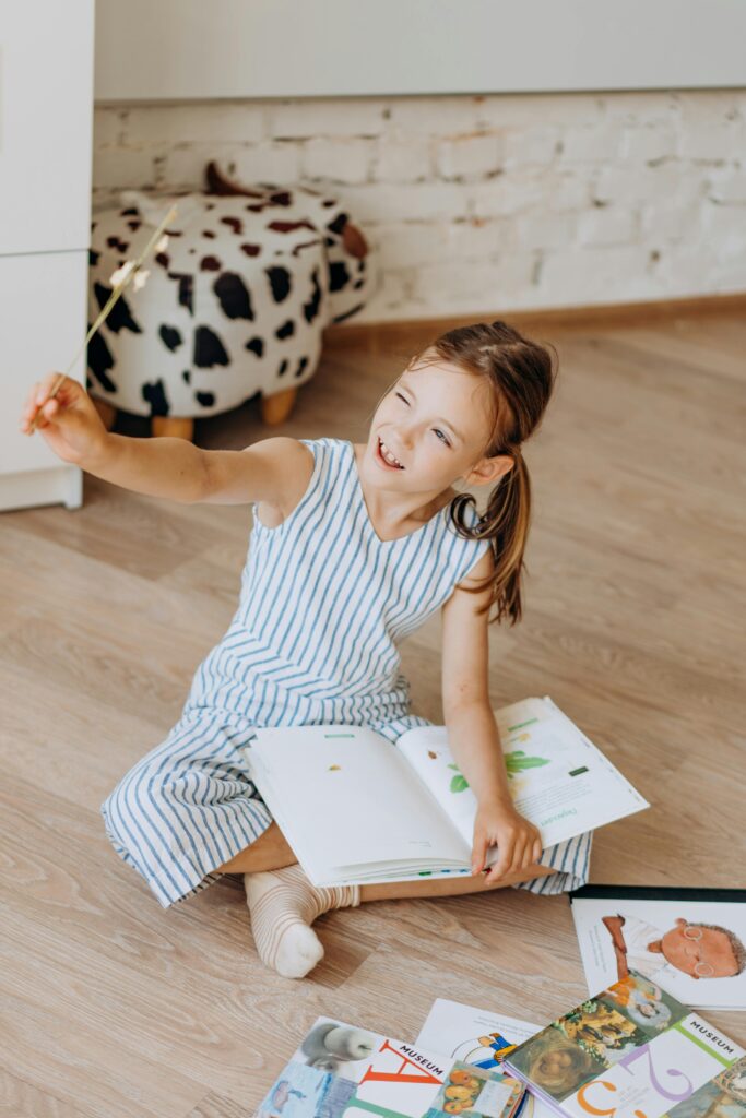 pexels photo 8923584 8923584 A smiling girl enjoying reading books on the floor indoors, exuding happiness and curiosity.
